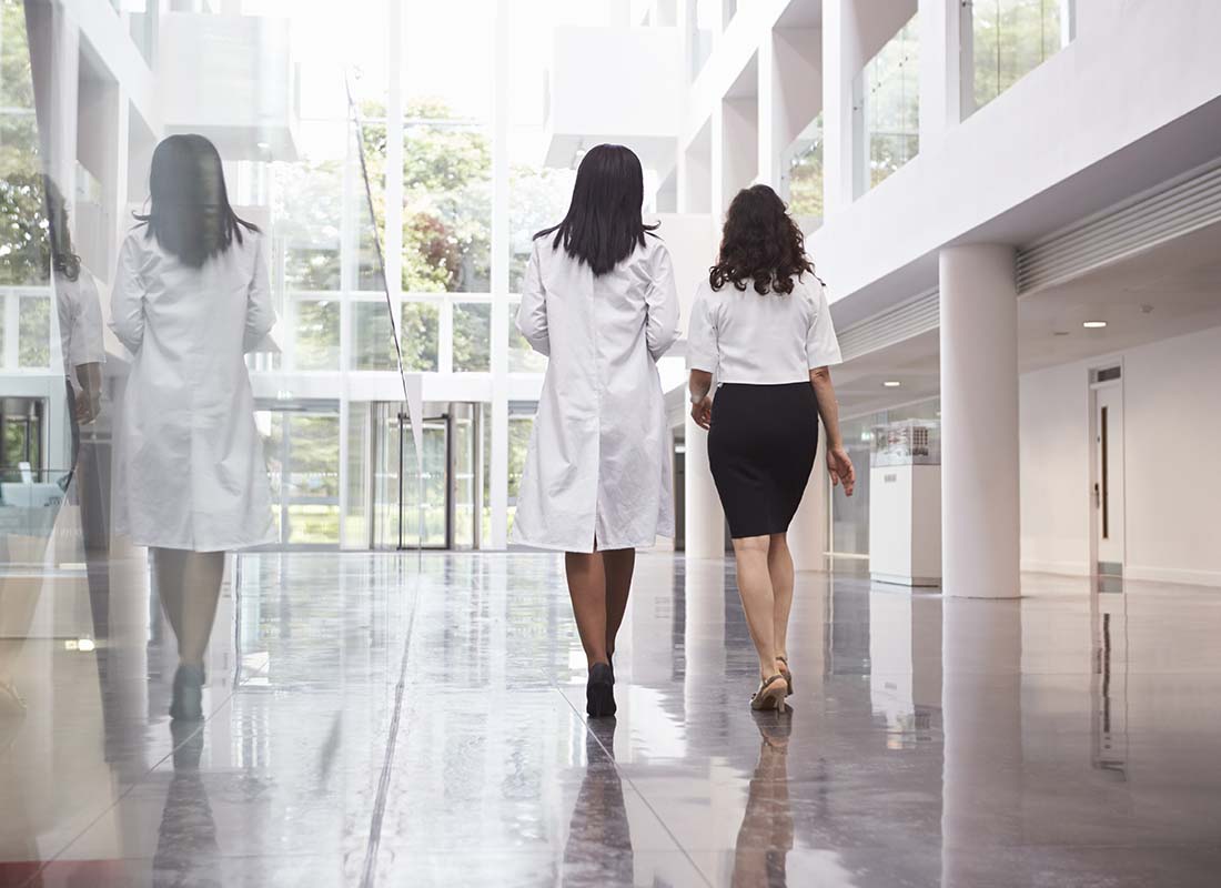 Group Hospital Insurance - Rear View of Doctors in a Modern Hospital as They Walk Away through the Hospital and Towards the Elevator