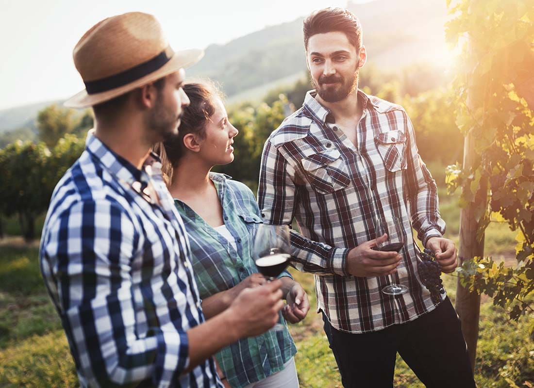 Winery Insurance - Wine Grower and Friends Walking through a Vineyard Drinking Wine and Tasting Grapes at Sunset